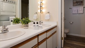 A bathroom with a double sink, a mirror with lights, a potted plant, and a toilet. - Outpost: Balsam Lodge A3 - Aspens Location! (Wilson)