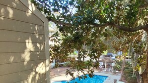 A pool area with lounge chairs and a table, surrounded by trees. - Condo Near Coligny Circle, Beach, & New Park; all within 1 to 2 Blocks (Hilton Head Island)