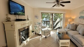 A living room with a fireplace, a television, a sofa, and a painting of a beach scene. - Condo Near Coligny Circle, Beach, & New Park; all within 1 to 2 Blocks (Hilton Head Island)