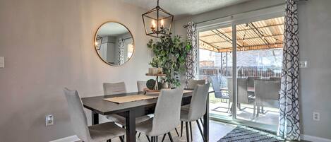 Un comedor con un espejo redondo, una lámpara colgante hexagonal y una mesa de comedor con sillas.