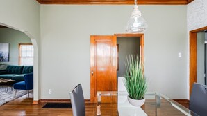 Un comedor con una mesa de vidrio, sillas, una planta en maceta y una puerta de madera al fondo.