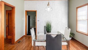 Un comedor con mesa de vidrio, sillas, lámpara colgante y papel tapiz estampado.