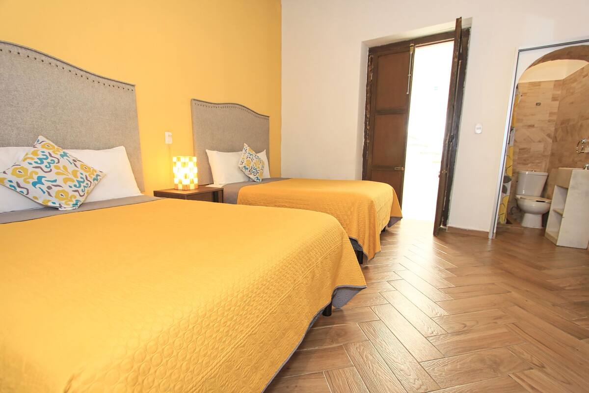 Een hotelkamer met twee bedden, houten vloeren en een badkamer die door een open deur zichtbaar is.