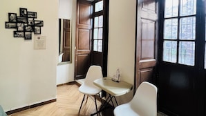 Une pièce avec un plancher en bois, un mur blanc orné de photos encadrées, une porte en bois et deux chaises blanches.
