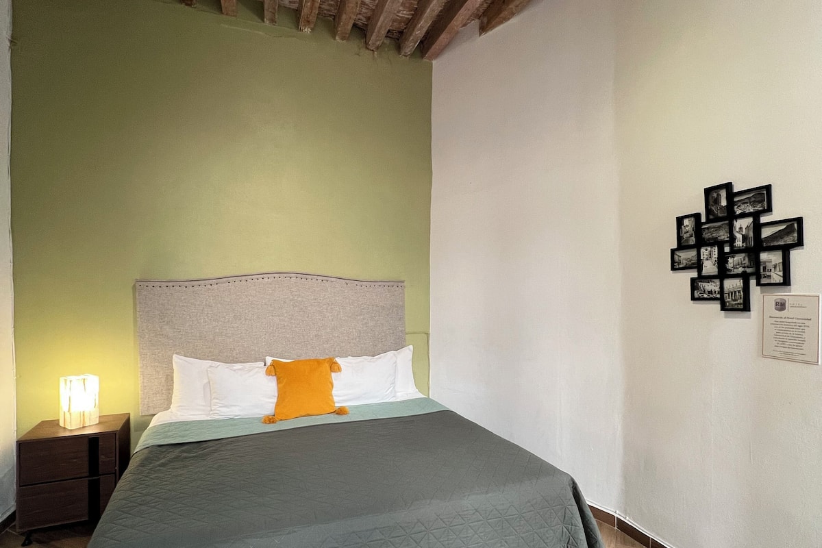 Een slaapkamer met een bed, houten vloer, groene wanden, een hoofdeinde en een nachtkastje met een lamp.
