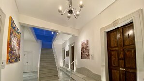 Un couloir avec un escalier, un lustre et une porte en bois portant le numéro « 1 ».