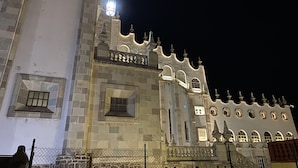 Un bâtiment historique doté d’une tour imposante et de fenêtres en arc de cercle, avec une façade en pierre et un balcon agrémenté de balustrades.