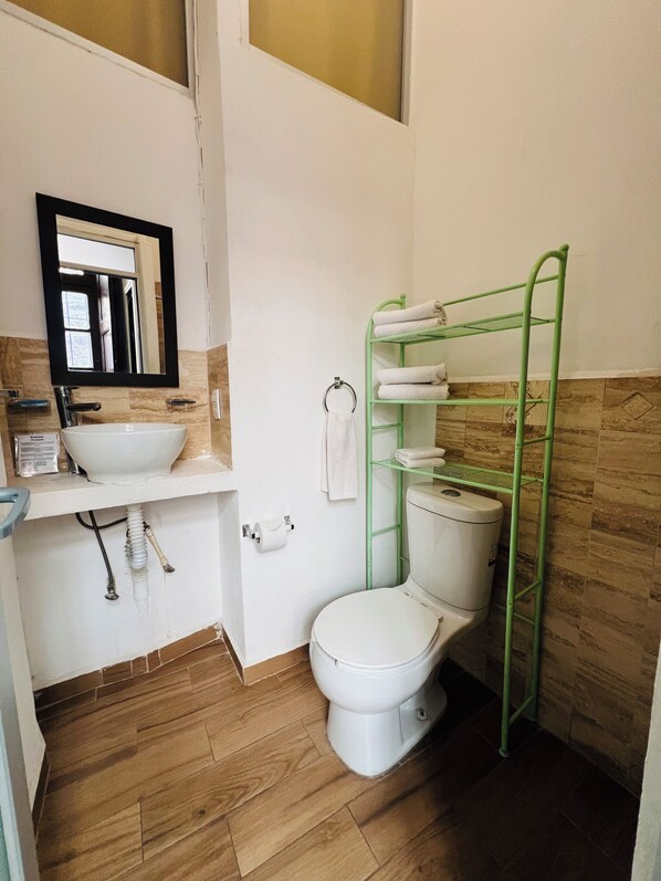 A bathroom with a white sink, a mirror, a toilet, a towel rack, and a green towel rack.