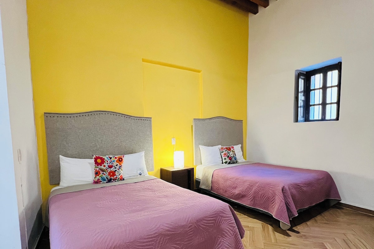 Een kamer met twee bedden, houten vloeren, een gele wand en een raam.