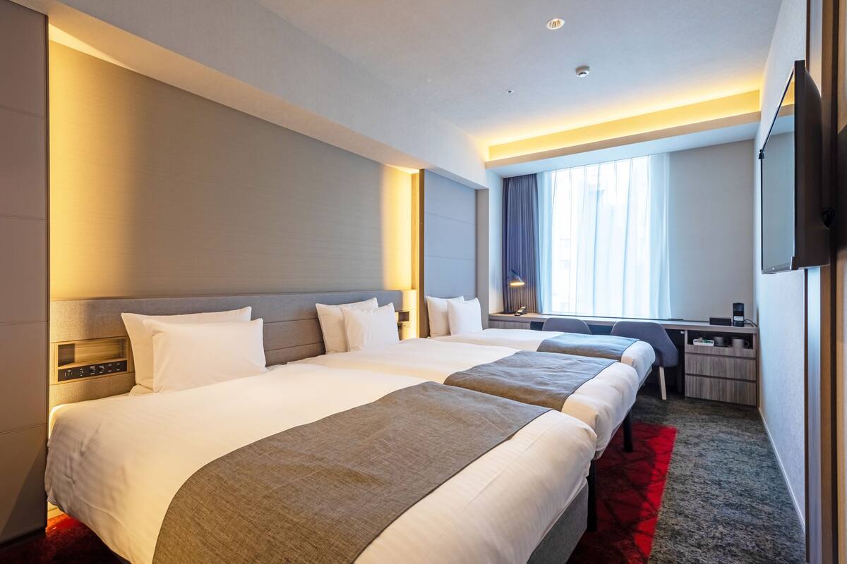 Une chambre d’hôtel avec deux lits, un bureau, une télévision et une fenêtre avec des rideaux.