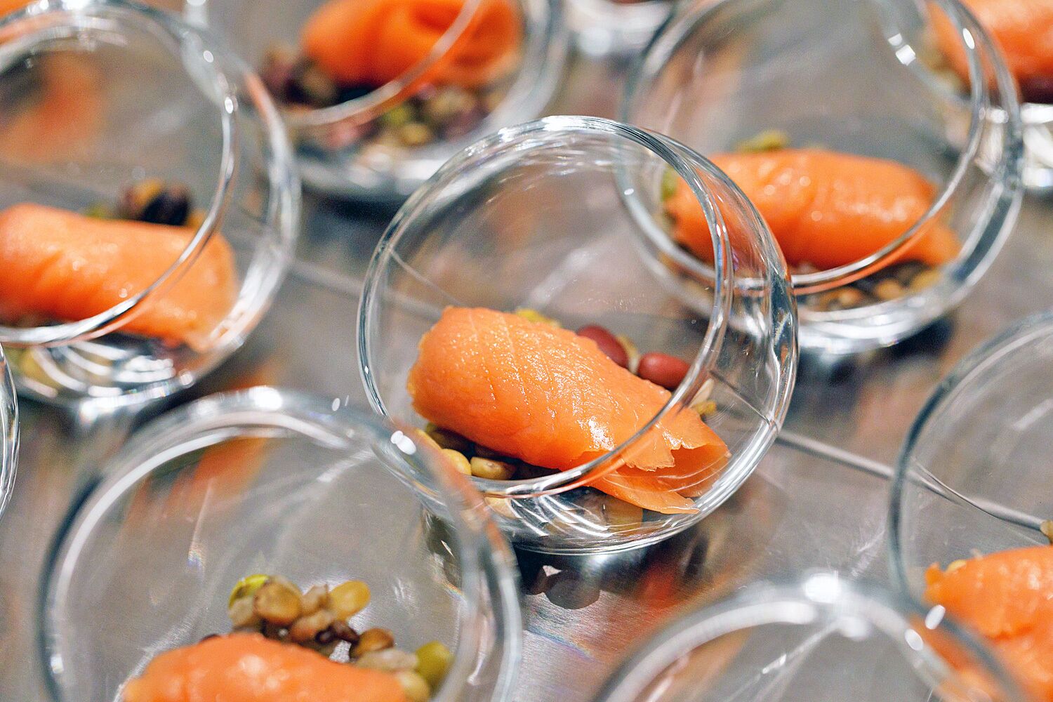 A series of clear glass dishes containing a food item, likely a type of appetizer or dessert, with a garnish of nuts and seeds.