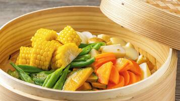 A bamboo steamer containing various vegetables like corn, green beans, carrots, and potatoes.