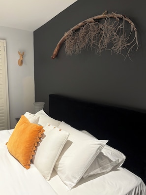 Un lit avec des oreillers blancs et moutarde, une tête de lit sombre et une décoration murale en forme de branche.