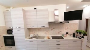 Een moderne keuken met lichte houten kastjes, een inbouwmagnetron, een roestvrijstalen spoelbak en een flatscreen televisie bevestigd boven het aanrecht.
