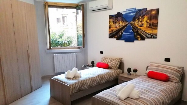 Een slaapkamer met twee bedden, een raam en een kunstwerk aan de muur.