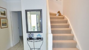 Un pasillo con un espejo, una pequeña consola y una escalera decorada con una figura de perro.