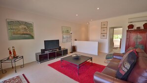 Una sala de estar con televisor de pantalla plana, un tapete rojo, un sofá de cuero y un mueble con objetos decorativos.