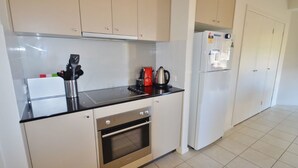Una cocina con gabinetes blancos, encimera negra, horno de acero inoxidable y refrigerador blanco.