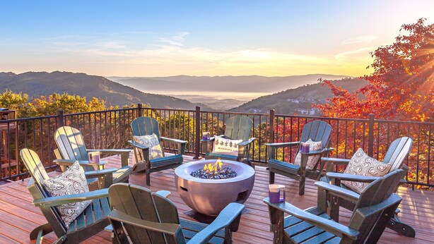 A deck with Adirondack chairs and a fire pit, overlooking a mountainous landscape.