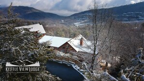 A lodge with a snow-covered roof, surrounded by mountains and trees.