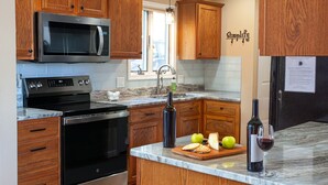 A kitchen with wooden cabinets, a stainless steel microwave, a black oven, a marble countertop, a sink, and a refrigerator.