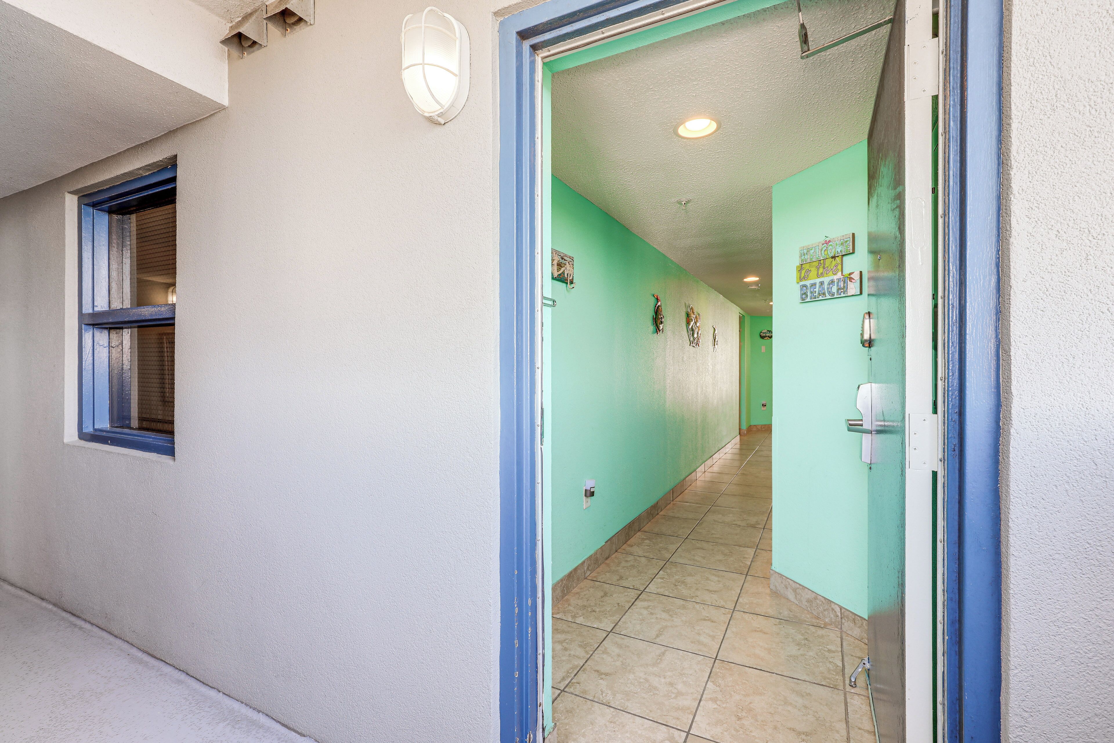 Un pasillo con pared verde, ventana con detalles azules y puerta con marco azul.