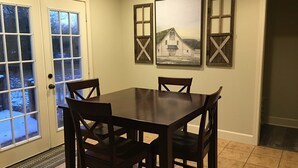 Un coin repas comprenant une table et quatre chaises, une porte avec des panneaux de verre et trois tableaux encadrés accrochés au mur.