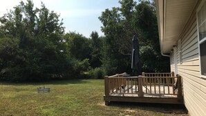 Un jardin avec une terrasse en bois, un barbecue et un parasol.