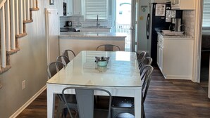 A modern kitchen with white cabinetry, a dining area with a glass table, and a staircase with a white railing.
