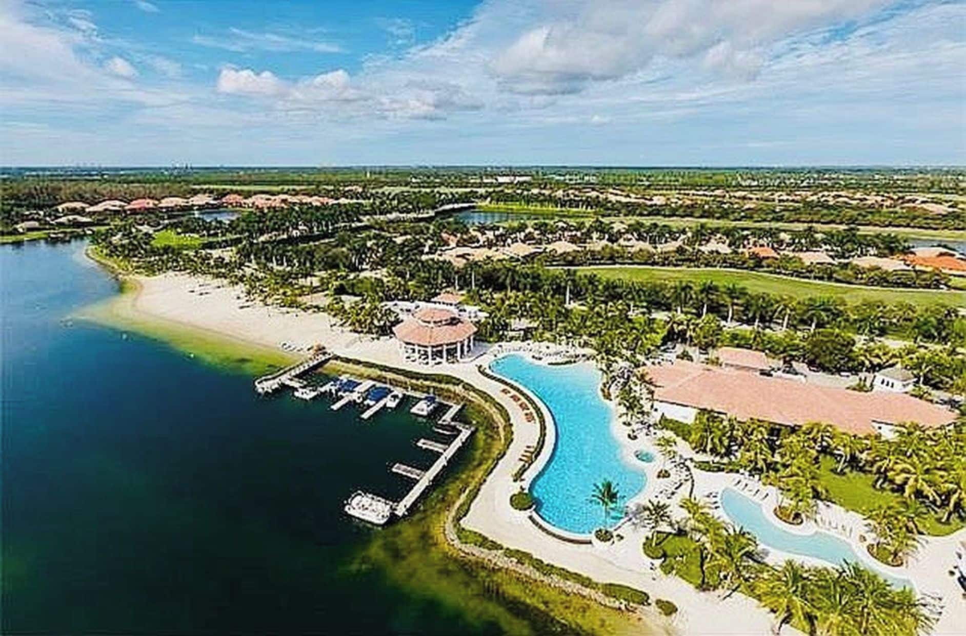 An aerial view of a resort with a large swimming pool, a marina, and lush greenery.