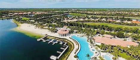 An aerial view of a resort with a large swimming pool, a marina, and lush greenery.