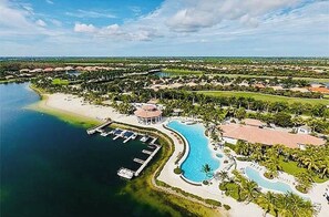 An aerial view of a resort with a large swimming pool, a marina, and lush greenery.