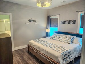 Et soveværelse med en seng, en fiskedekoration på væggen, et skilt med teksten 'EAT SLEEP FISH' og et vindue med gardiner.