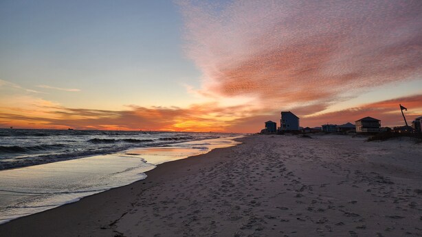 A beach with footprints leading to the water, a clear sky, and buildings in the background.