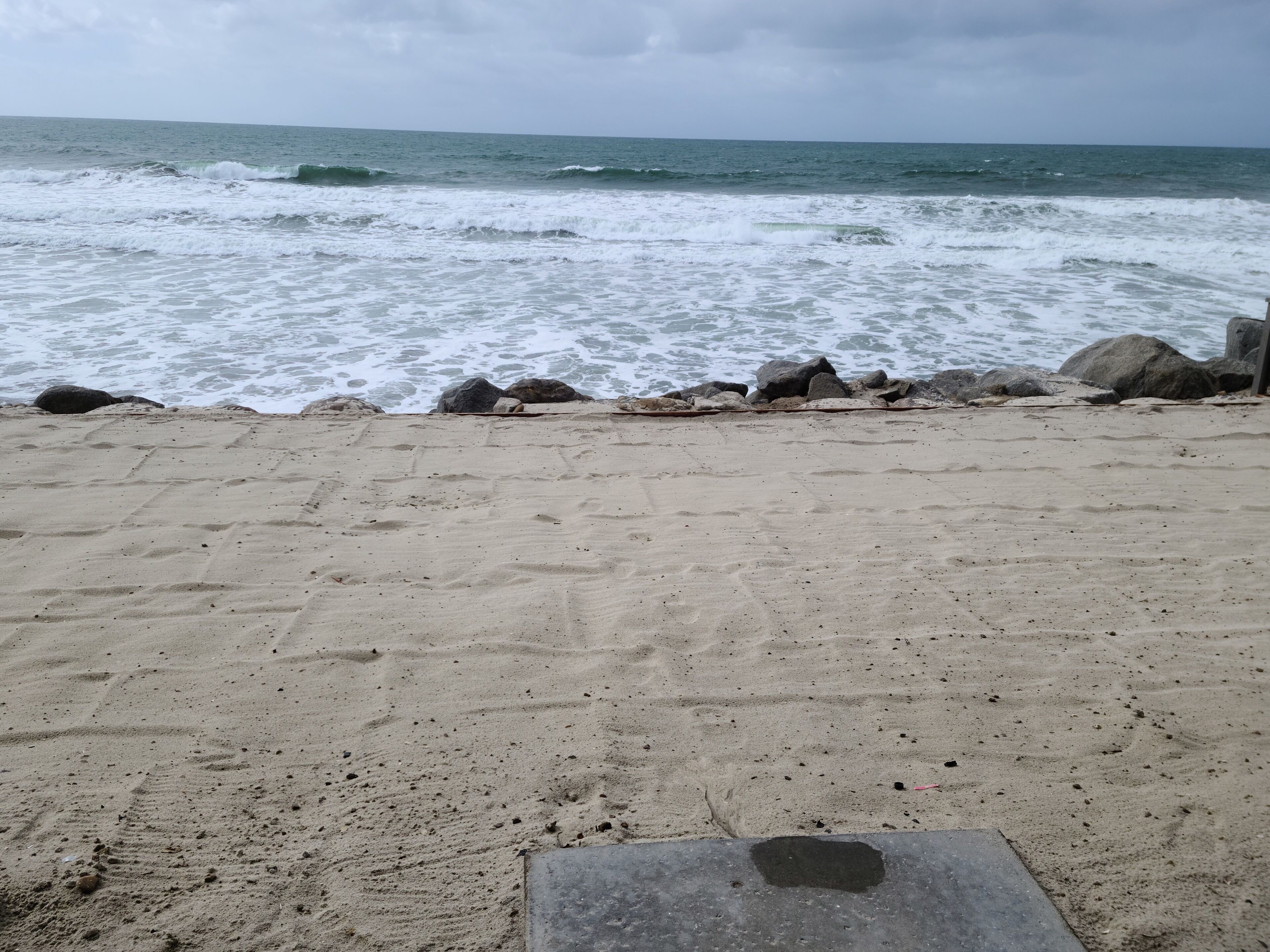 En sandstrand med bølger der slår mod klipper.