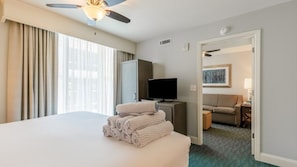 A hotel room with a large bed, a television, a desk, and a view of the outside through the window. - North Myrtle Beach | Family Wave Hub | Pool + Beach | 3BR | Sleeps 10 (North Myrtle Beach)