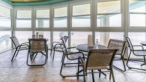 Ein Zimmer mit großen Fenstern, Korbstühlen, einem runden Tisch und einem Fliesenboden.