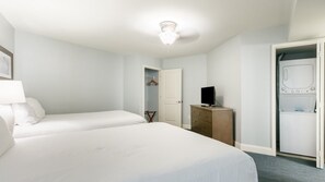 Ein Hotelzimmer mit zwei Betten, einem Schminktisch, einem Fernseher und einer Waschgelegenheit.