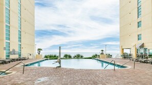 A pool area with a view of the ocean, surrounded by a brick patio and lounge chairs.