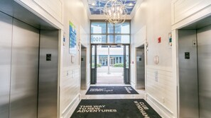 A modern elevator lobby with a clear view of the entrance, a black mat with text, and a ceiling light fixture.