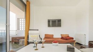 Een moderne woonkamer met een witte bank, een glazen tafel en een aan de muur bevestigde televisie.