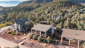 A modern two-story house with a large deck, surrounded by a mountainous landscape.