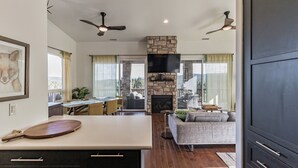A modern kitchen with a stone fireplace, dining area, and a living room with a sofa and TV.