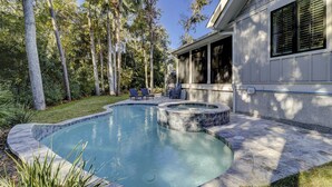 Une piscine avec un jacuzzi, entourée d’une terrasse dotée de chaises et d’un espace abrité.