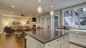Une cuisine spacieuse dotée d’un grand îlot central, de meubles blancs et offrant une vue sur l’extérieur grâce à de grandes fenêtres.