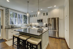 A modern kitchen with a large island, stainless steel appliances, and a view of the outdoors through large windows.
