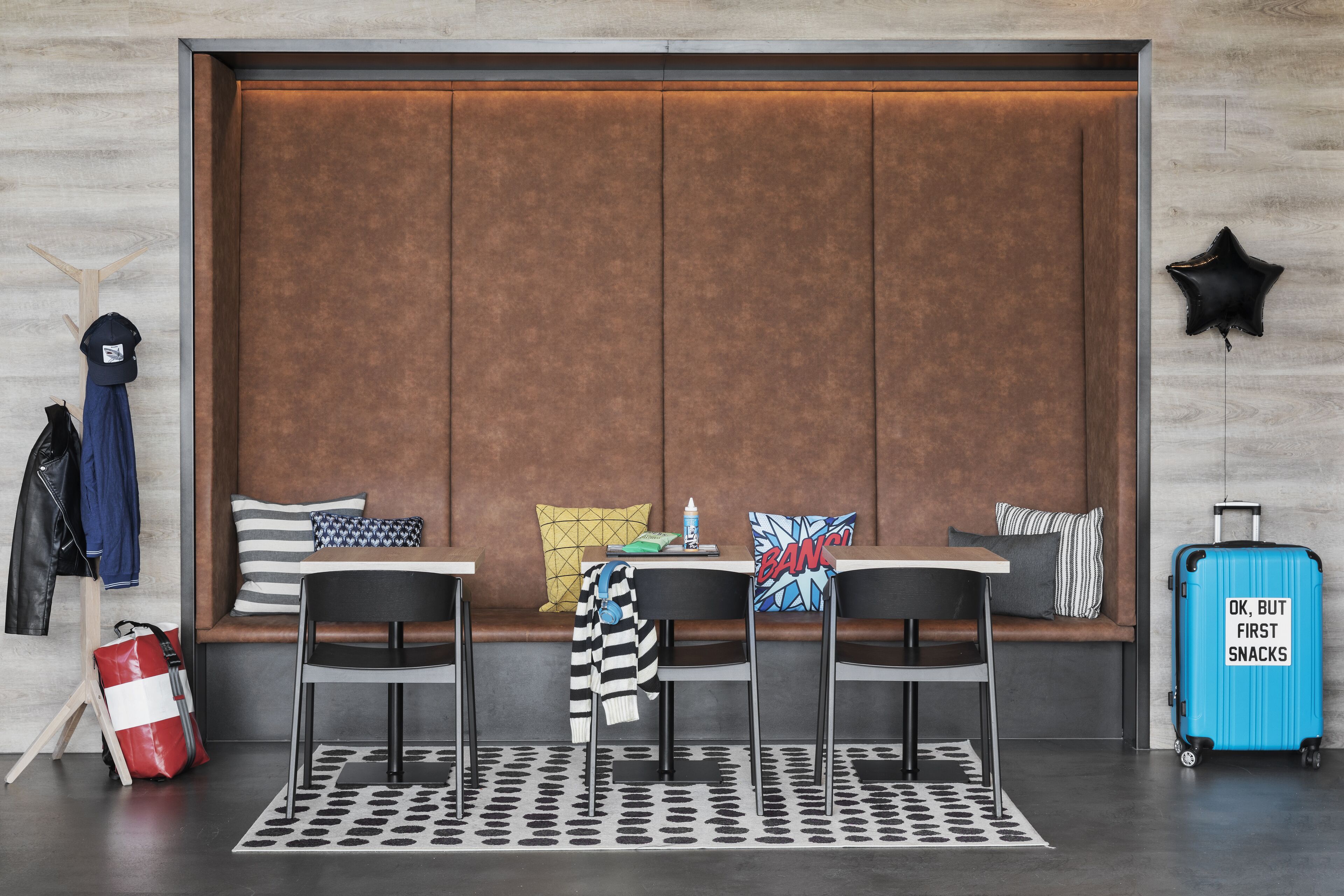A modern hotel room with a large cushioned seating area, a small table, and a suitcase.