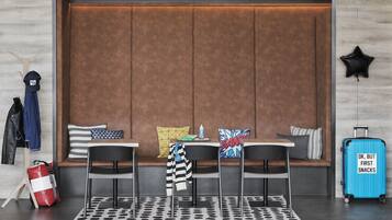 A modern hotel room with a large cushioned seating area, a small table, and a suitcase.