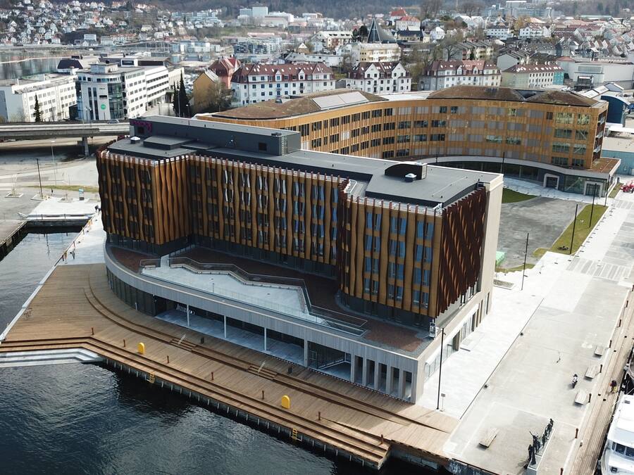 Un edificio moderno con fachada curva, un muelle frente al agua y un estacionamiento con barcos.