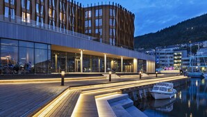 Un hotel moderno frente al agua, con muelle de madera, fachada de vidrio y vistas al agua y a las embarcaciones.